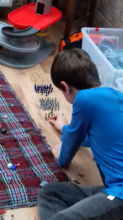 A boy, seen from behind, arranging rows of toy soldiers on the floor at home