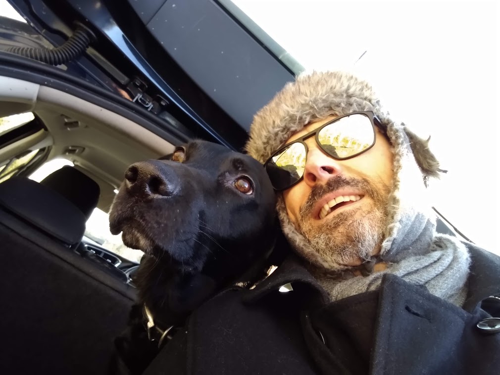 Joe in a winter hat, cheek to cheek with Maïka, his black therapy dog