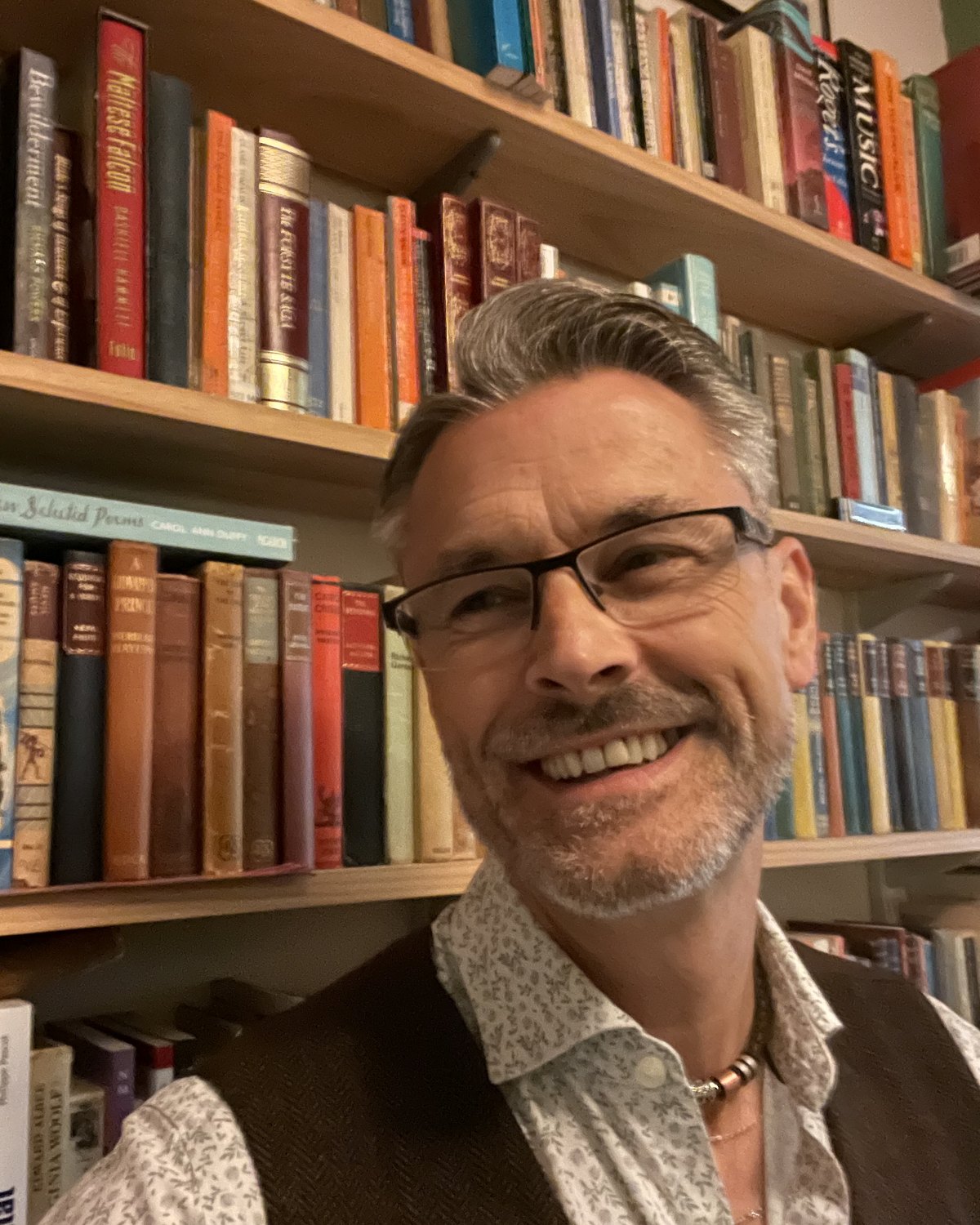 Joe Maingot, smiling, in front of a wall of bookshelves at home